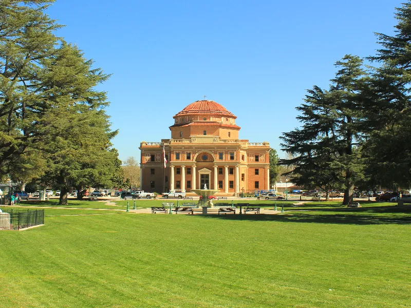 Historic domed building with columns, surrounded by trees and a green lawn under a clear blue sky.