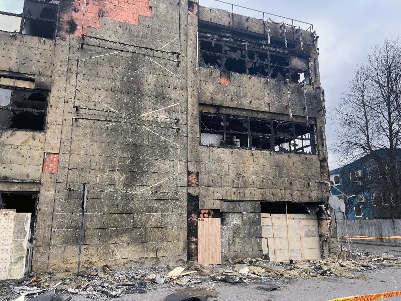 Burned and damaged multi-story concrete building with shattered windows and debris on the ground.