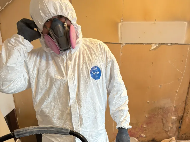 Person wearing a white Tyvek protective suit and respirator mask indoors.