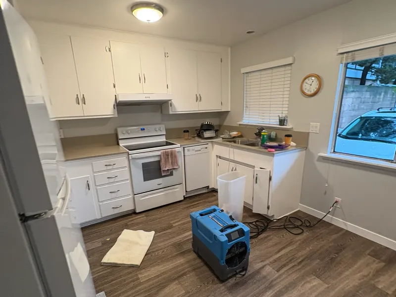 Kitchen with white cabinets, a stove, and a blue air mover on the floor.
