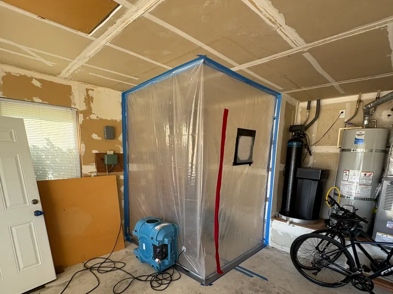 Plastic containment tent with an air scrubber inside a garage.