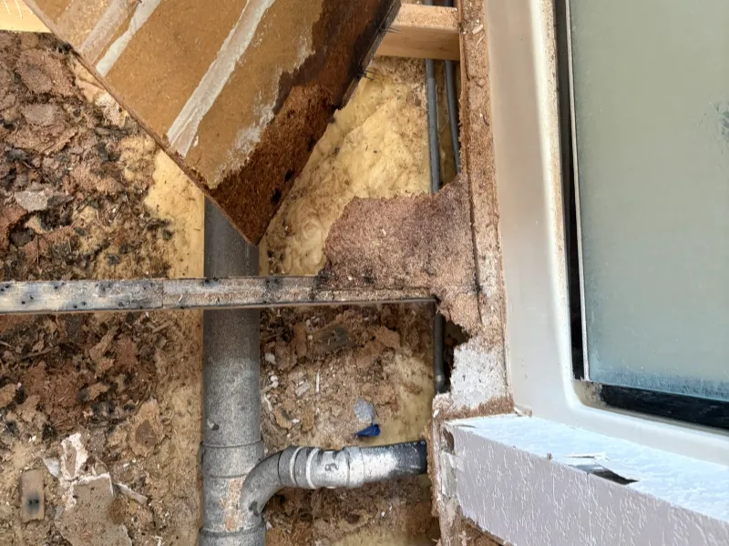 Exposed plumbing and damaged wall insulation near a window frame.